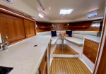 Yacht cabin: white U-shaped seating around a wooden table, with teak floors and warm wood cabinets.