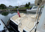 Rear seating area of a white powerboat with beige cushions, American flag at the stern, dock and calm marina in view.
