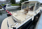 A white luxury motorboat docked at a marina with beige seating and an American flag at the stern while another boat rests nearby.