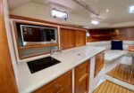 Compact yacht galley with white speckled countertop, electric stove, and built-in microwave above wooden cabinets.