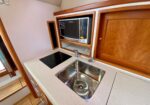 Galley kitchen with a stainless sink, electric cooktop, and built-in microwave in a wooden cabinet area on a boat or small space.