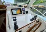 Boat helm with a touchscreen navigation display showing a map, plus engine gauges and throttle in a white glossy cockpit interior with wooden wheel rim nearby.