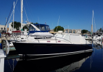 Dark navy motor yacht docked at a busy marina with other sailboats and blue sky above.