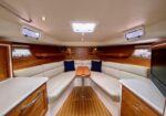 Luxurious boat salon with white cushioned U-shaped seating, wooden panels, and a polished wooden table in the center of a cabin ship interior.