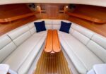 U-shaped beige leather seating around a teak table in a boat cabin with navy cushions and warm wood paneling.