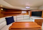 Cozy boat cabin with cream leather seating, a wooden table, and a flat-screen TV built into wood cabinetry.