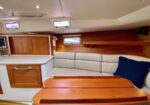 Cozy boat cabin with white leather seating, wooden cabinets, and a varnished dining table under small porthole windows.