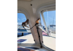 Close-up of boat cabin window latches with wooden handles and metal supports, marina seen outside the windows.