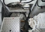 Industrial mechanical room view showing hoses, pumps, and a white Bosch component mounted near the ceiling area above a diamond-plate access panel.