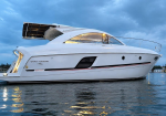 White luxury motor yacht anchored on calm water, viewed from the side with an open upper deck and railing lighting at dusk