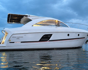 2015-B2 | Boat Universe White luxury motor yacht anchored on calm water, viewed from the side with an open upper deck and railing lighting at dusk