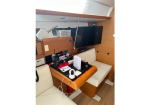Boat cabin workspace with a wooden desk, two white cushioned seats, a wall-mounted TV, and radio/monitor equipment on the desk.