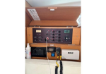 Wooden marine control panel with gauges, switches, and a wired VHF handheld mic mounted in a boat console; a small white B&G unit sits nearby and a spray bottle is on the left.