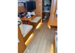 Wood-paneled yacht cabin with beige seating, a small desk, TV, and a doorway to a compact head; warm floor lighting along the baseboards.