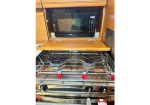 Microwave oven mounted in a wooden cabinet above a stainless steel gas stove with metal grates and red control knobs.