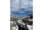 Sailboats docked side by side in a marina, masts rising against a partly cloudy blue sky; white hulls with fenders along the docks.
