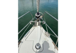 View from the bow of a sailboat, showing the deck, railing, and windlass with calm green water ahead.