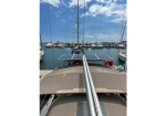 View from the cockpit of a sailboat toward a marina, with a solar panel mounted on a pole and masts in the background.
