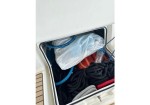 Open boat storage locker with coiled black ropes, a plastic bag, a blue hose, and a water bottle inside the compartment.