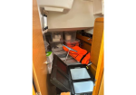 Interior of a small cabinet cluttered with emergency gear: orange life jacket, plastic bins, and various containers under a countertop.