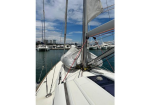 View from the deck of a sailboat at a marina, with furled sails and rigging against a blue sky and calm water.