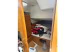 Compact boat cabin with a lower bunk, wooden cabinet, and clutter including a backpack and clothes; a water bottle sits on the floor.