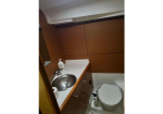 Small bathroom with a rounded stainless sink, soap bottle, wooden storage cabinets, and a closed toilet.