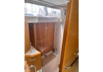 Small compact bathroom with a glass shower enclosure, wooden cabinet, and a sink, seen from the doorway.