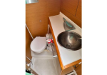 Compact bathroom: white toilet on the left and a round stainless sink in a wooden cabinet on the right, with cleaning brushes and a toilet brush nearby.