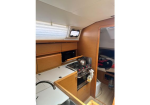 Boat galley with sink, stove, kettle, wooden cabinets, and a doorway to a sleeping berth