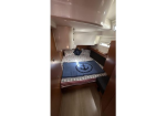 A compact boat cabin with a bed, blue anchor-themed bedspread, and wooden cabinetry along the walls