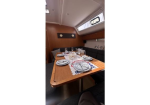 Wooden dining table in a sailboat cabin set for a meal with plates, glasses, and cutlery, surrounded by dark seating and a window.
