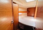 Cozy wooden boat cabin with a built-in curved bed, wood paneling, storage cabinets, and a skylight above.