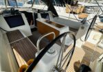 Sleek cockpit of a modern sailboat with a teak deck, wheel, and a wooden center table amid navigation screens and seating.