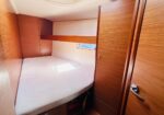 Compact wooden cabin bedroom with a single bed, built-in wardrobe, and small window on the wall ahead.