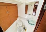 Compact boat bathroom with wooden cabinets, a white toilet, and glass vessel sink under a mirror.