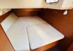 Wood-paneled boat cabin with a V-shaped double bed and white cushions under a hatch window.