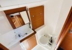 Compact boat bathroom with white sink, wooden cabinets, and a mirror, plus a toilet at the end right side.