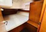Compact boat cabin with lower bunk bed, white mattress, and a tall wooden wardrobe against the right wall.