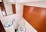 Compact boat bathroom with toilet, glass vessel sink, and wooden storage cabinets along the wall.