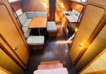 Interior of a wooden boat cabin with a U-shaped sofa, table, and stools by a compact kitchen area with sink and fridge on the right