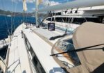 Sunlit sailboat deck with rigging and cushions, blue sea and distant mountains in the background.