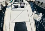 Top-down view of a white sailboat docked at a marina, with a small inflatable dinghy tied at its side and open cabin hatch windows nearby.