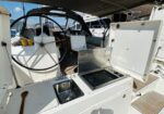 Open galley on a sailboat: stainless sink with wooden spoon, and a covered cooler/grill to the side, helm and seating aft under a shade canopy.
