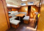 Sailboat cabin with an L-shaped sofa around a wooden table and light gray cushions, wood-paneled walls, and skylights above.
