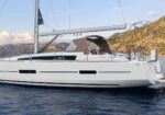 White sailing yacht on calm blue water with a beige canopy and cockpit seating, mountain coastline in the background
