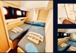 Interior of a boat cabin with two parallel twin beds, blue sheets, anchor-pattern towels, and wooden paneling. Porthole window visible on the left.