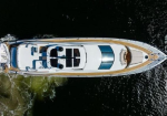 Top-down view of a white luxury motor yacht cruising in dark water, showing the sun deck, seating areas, and blue-tinted windows.