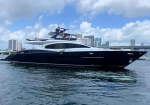 Dark-hulled luxury motor yacht on calm water with a city skyline in the background.