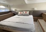 A luxurious yacht cabin with a large bed, gray and white bedding, and decorative pillows featuring orange starfish patterns.